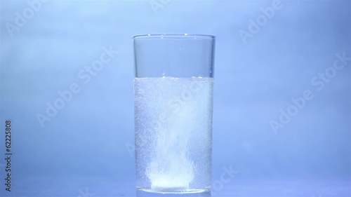 Tablet of sparkling aspirin in glass on  blue background photo