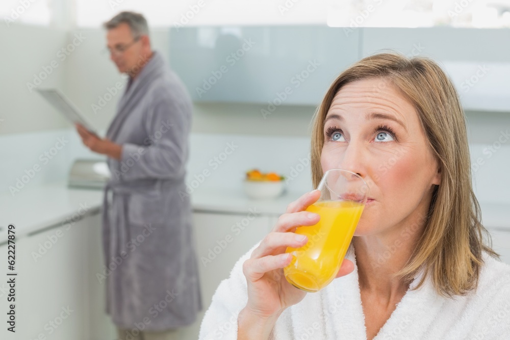 Woman drinking orange juice with man in background Woman drinking orange juice with man in background