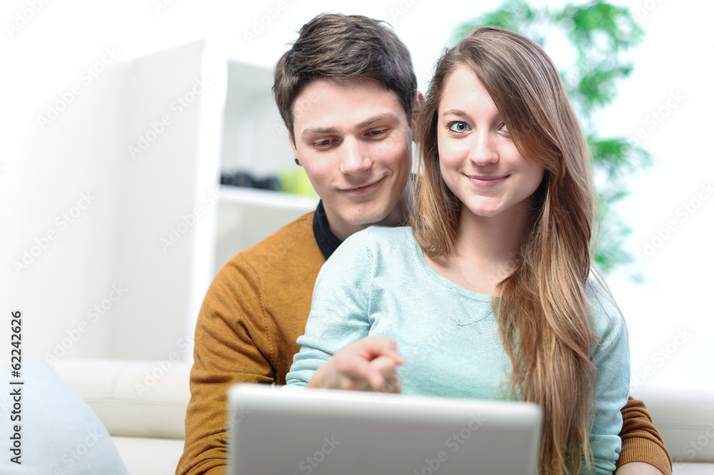 Portrait of a smiling young couple using laptop at home indoor Portrait of a smiling young couple using laptop at home indoor