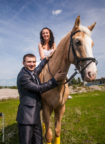 Handsome groom holding horse with bride in saddle by rein