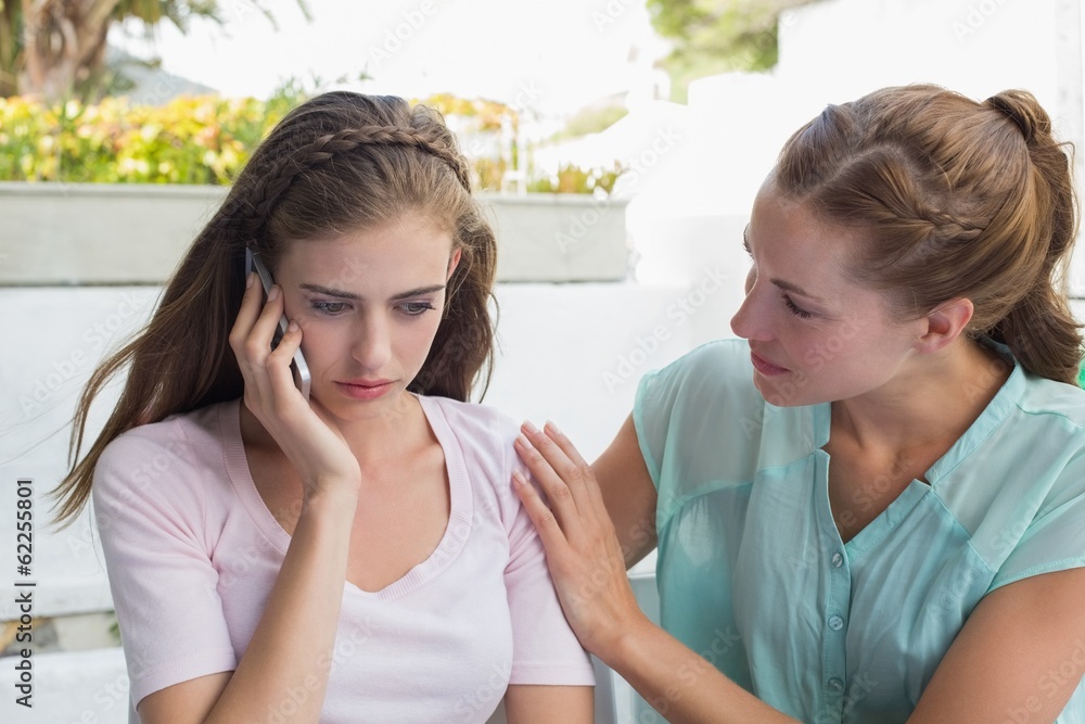 Woman consoling a friend while shes on call in café Woman consoling a friend while shes on call in café