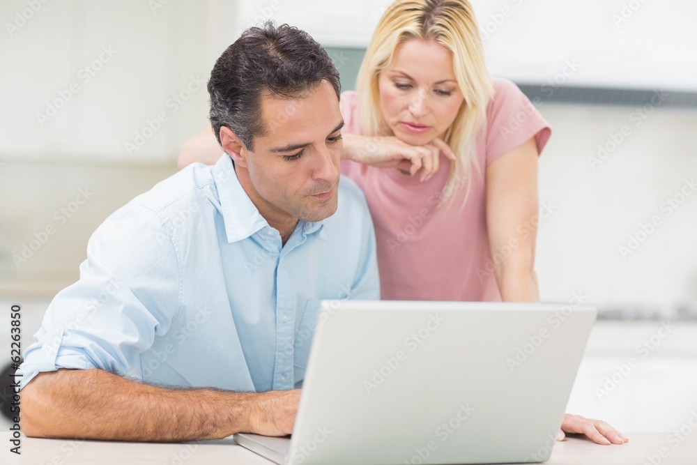 Concentrated couple using laptop in kitchen Concentrated couple using laptop in kitchen