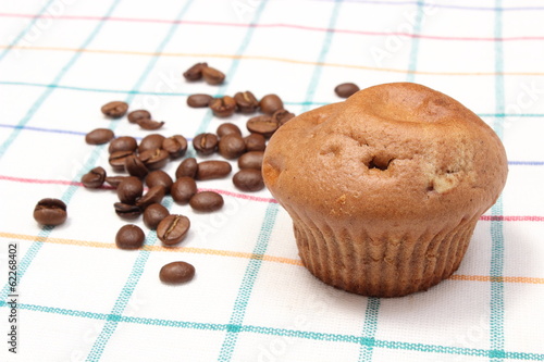 Fresh baked muffin and coffee grains on colorful cloth