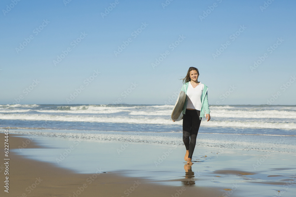 Tenage girl walking in the beach with her surfboard