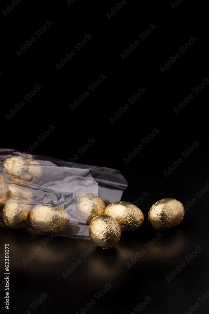 Obraz premium Chocolate mini eggs in a cellophane bag on a black background