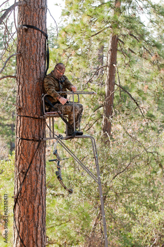 Bow hunter in a ladder style tree stand safely raising his bow with a haul line
