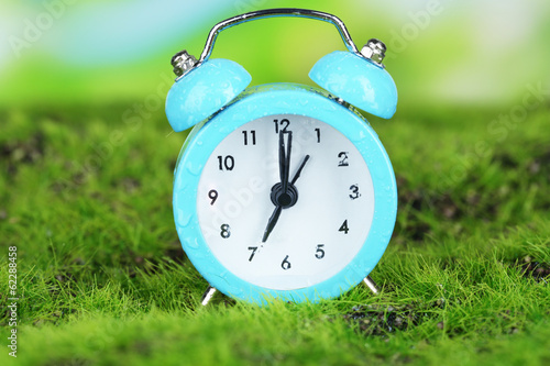 Blue alarm clock on grass on natural background