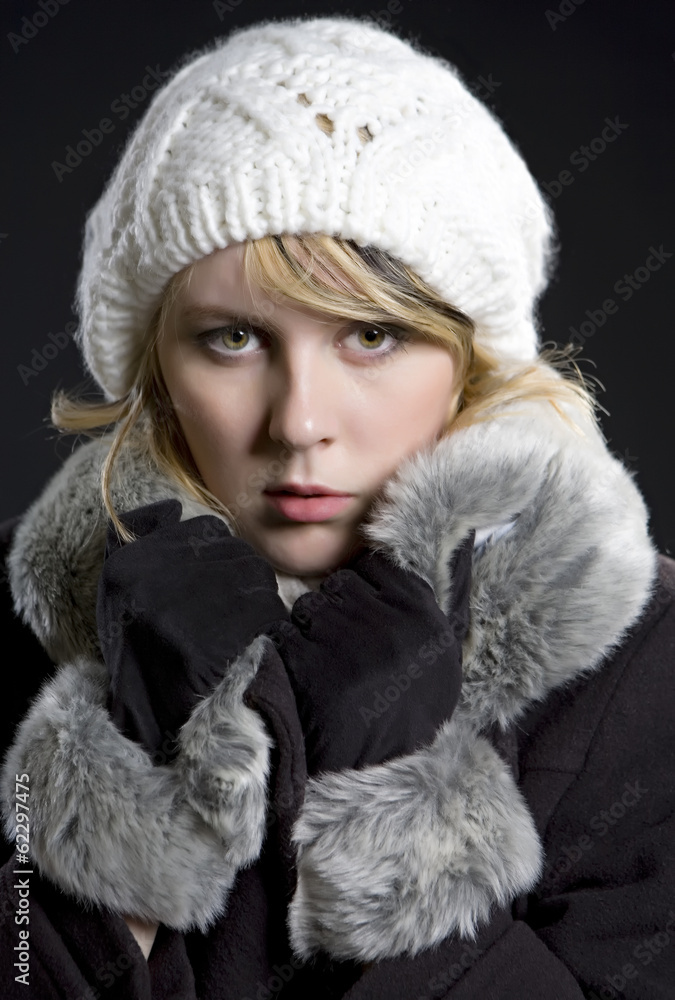 Girl in coat and white cap on black background. Winter, fur, col