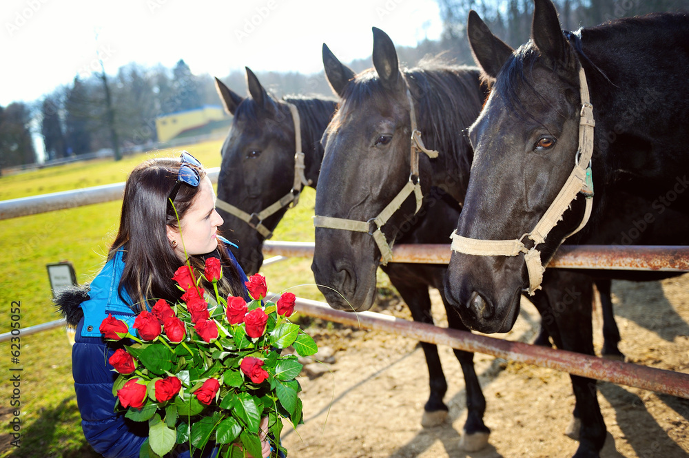 Obraz premium Beautiful young woman with bunch of roses and black horses