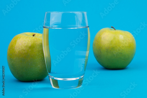 A glass with water and two green apples