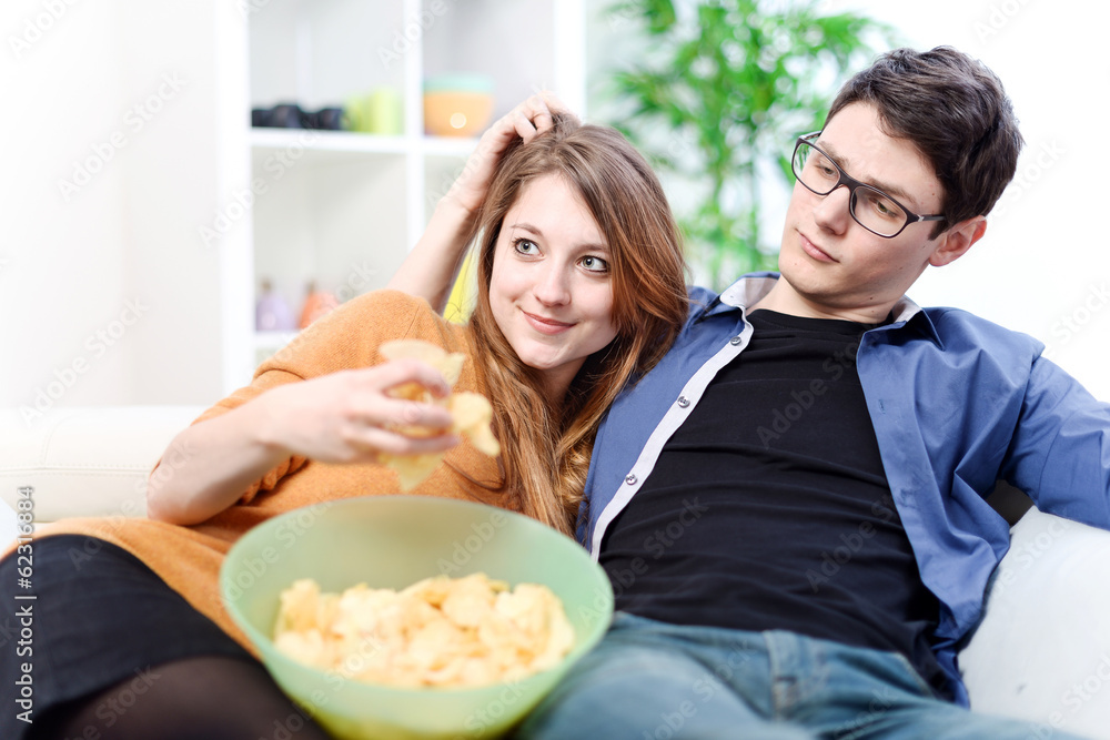 Beautiful young couple watching tv and eating on a sofa