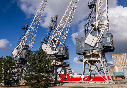 Horizontal color image of 3 old cranes in docks.