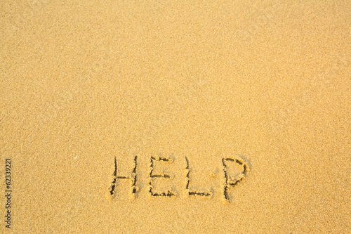 Help, written in sand on beach texture.