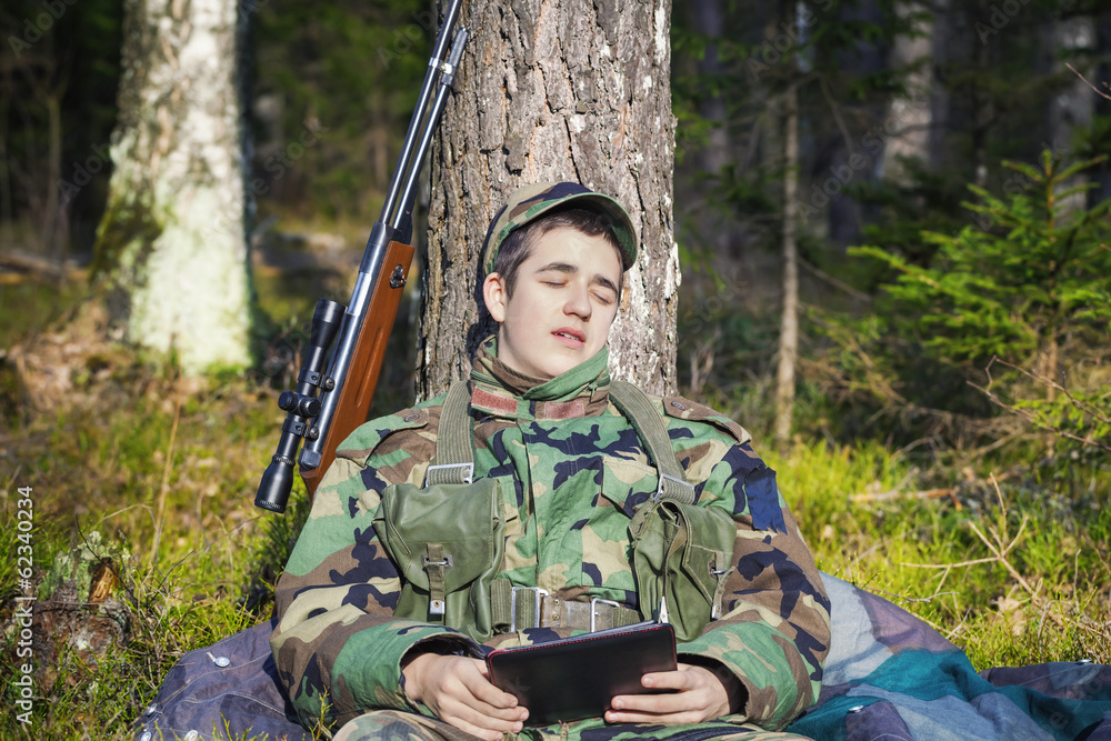 Sleeping recruit with tablet PC and optical rifle in forest