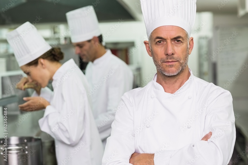 Serious chef looking at camera with team working behind Serious chef looking at camera with team working behind