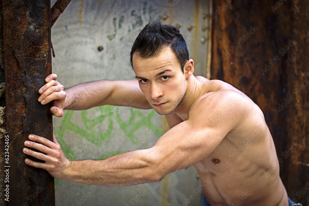 Muscular young man standing, leaning against rusty metal