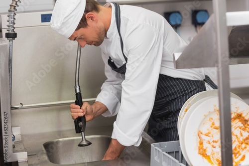 Kitchen porter cleaning plates in sink photo