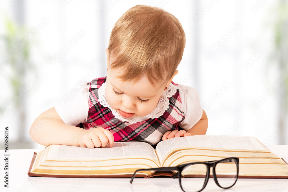 funny baby girl in glasses reading a book in a library funny baby girl in glasses reading a book in a library