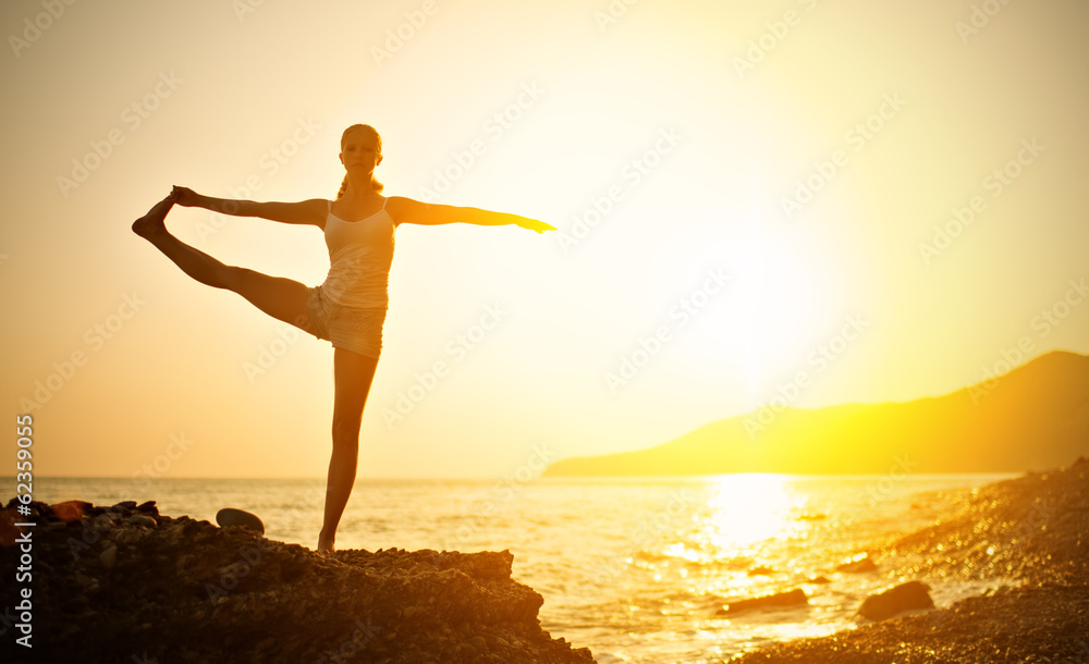 woman doing yoga on the beach at sunset