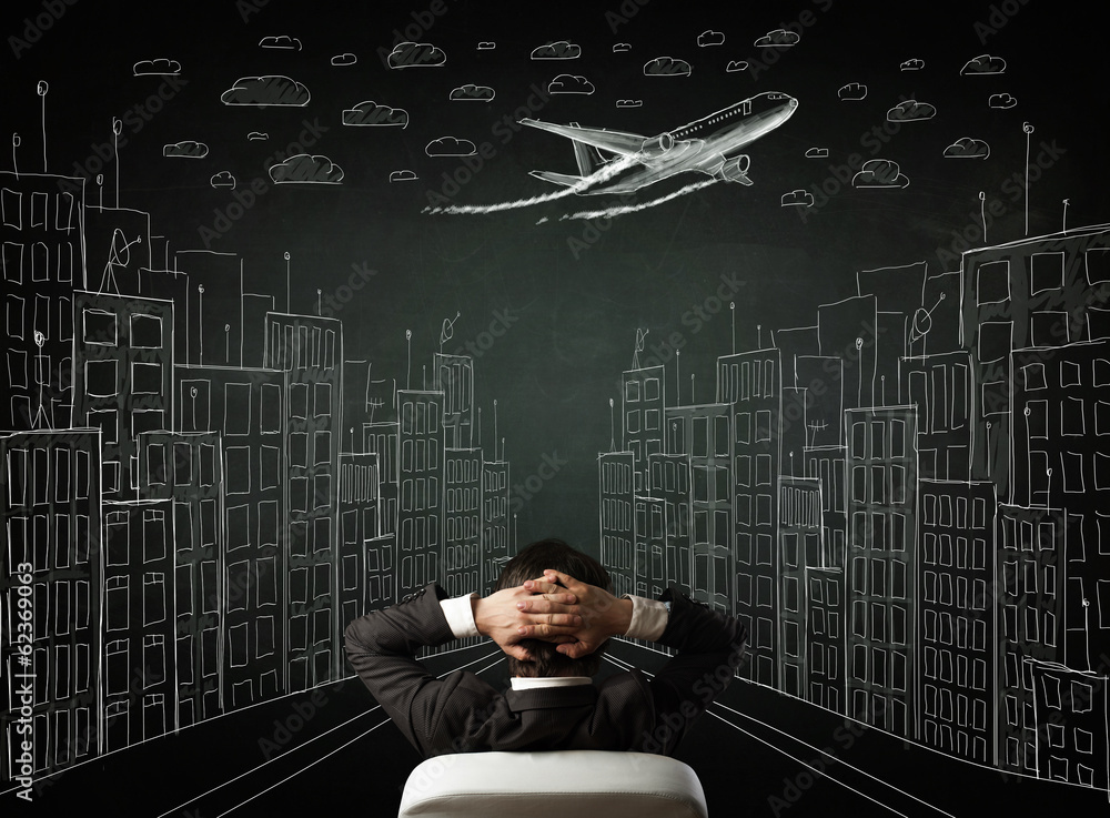 Businessman sitting in front of a cityscape drawing on a chalkbo Businessman sitting in front of a cityscape drawing on a chalkbo