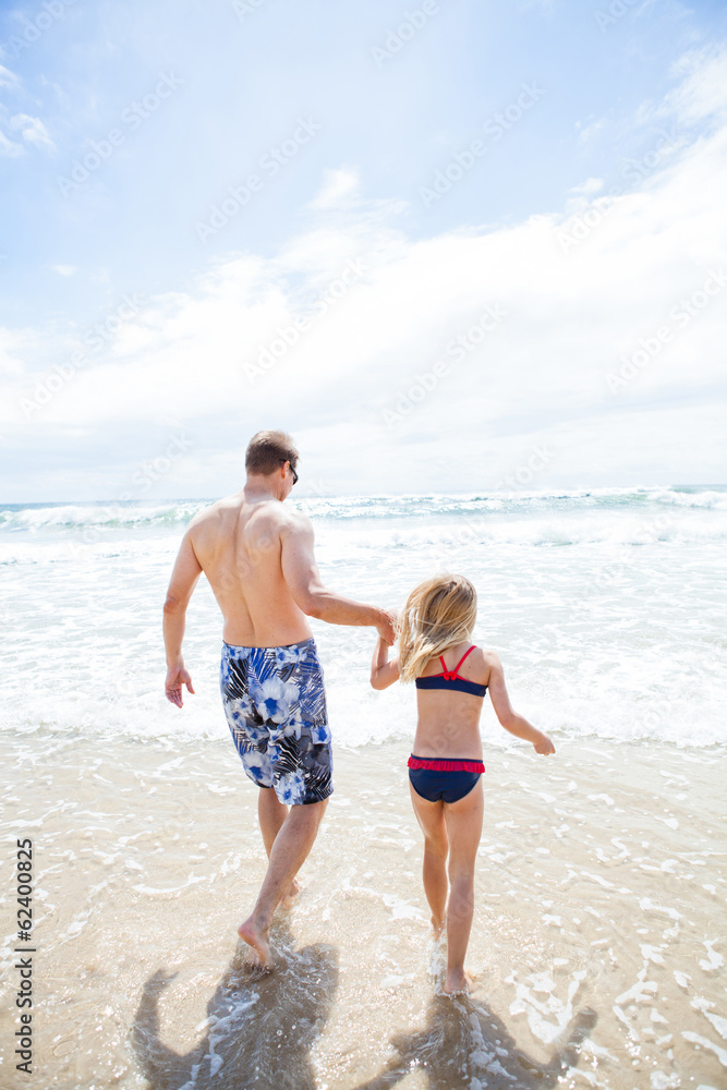 Father and young daughter walking into water at beach