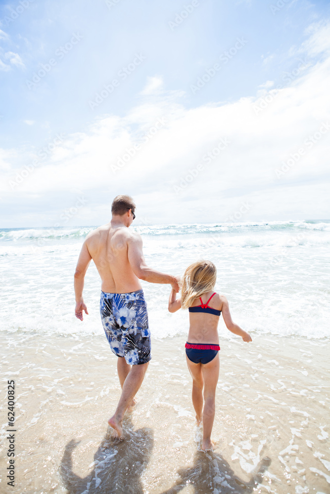 Father and young daughter walking into water at beach Father and young daughter walking into water at beach