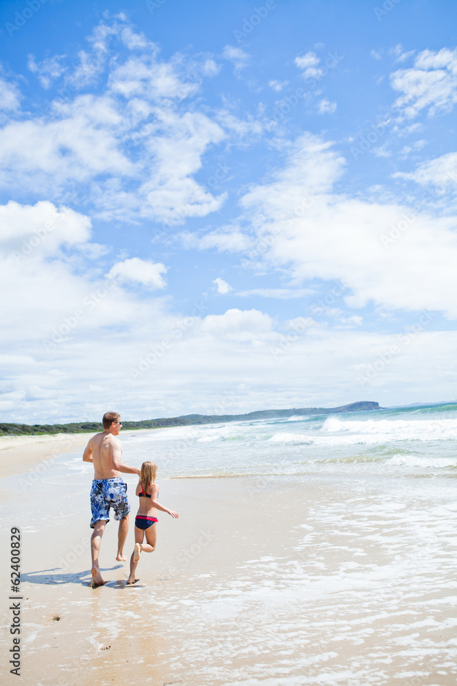 Father and young daughter running along beach