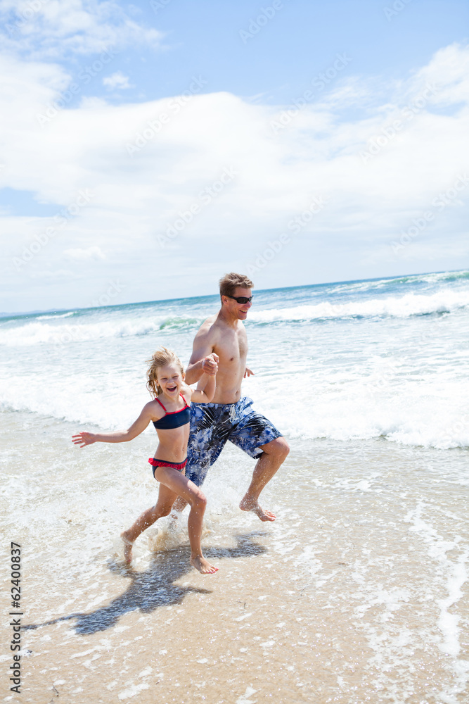 Happy father and daughter running along beach in shallow water Happy father and daughter running along beach in shallow water