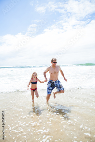 Happy father and daughter running from waves at beach