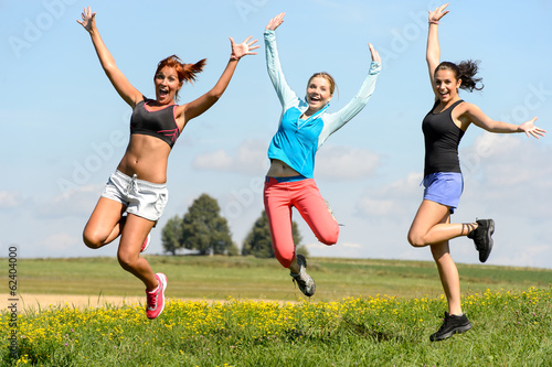 Sporty friends jumping cheerful on sunny meadow