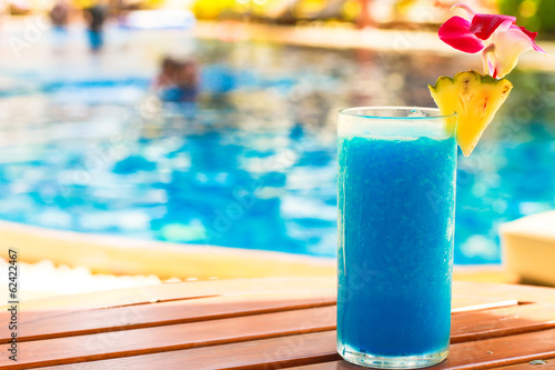 Tropical blue cocktail on woodem table near swimming pool photo