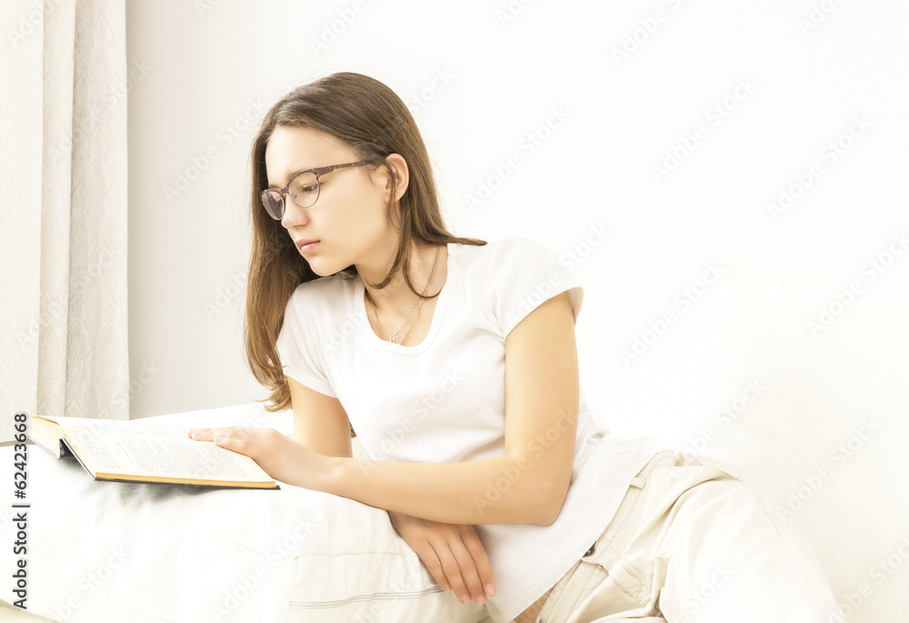 beautiful teen girl with glasses reading a book on the couch beautiful teen girl with glasses reading a book on the couch