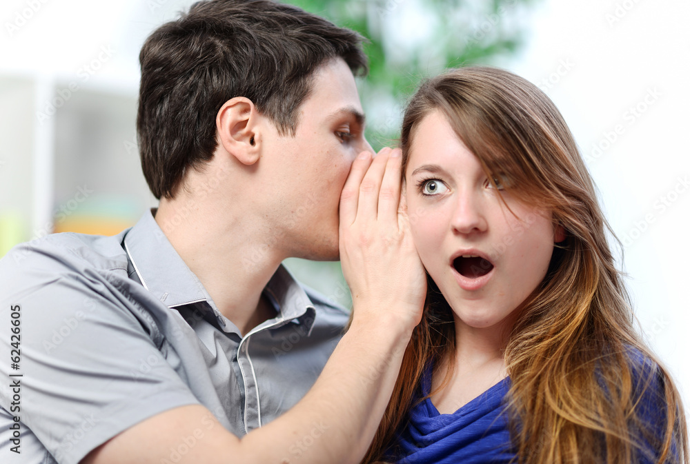 man whispering in the ear of his surprised wife man whispering in the ear of his surprised wife