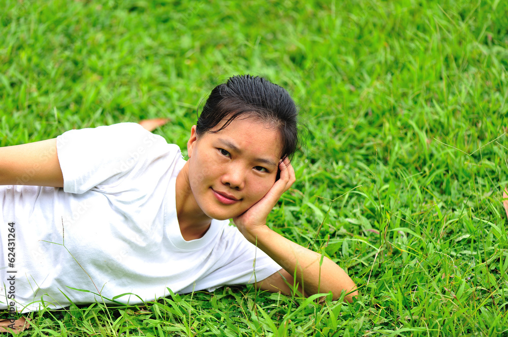 young aasian woman reading book laying down on green grass young aasian woman reading book laying down on green grass
