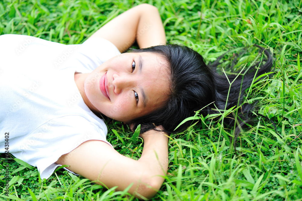 young aasian woman reading book laying down on green grass young aasian woman reading book laying down on green grass