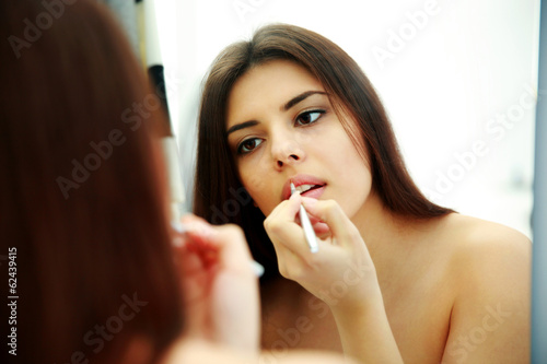 Young beautiful woman looking at mirror while doing makeup