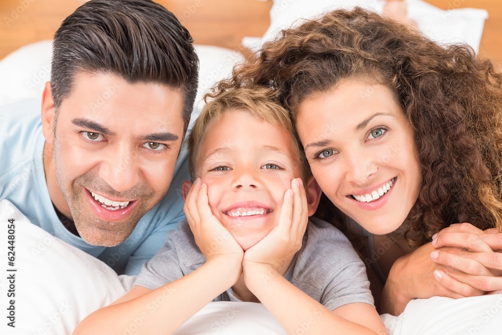 Cute young family lying on bed together smiling at camera