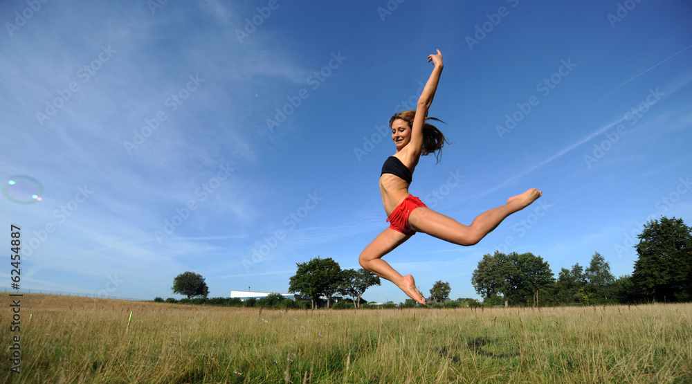 Frau in knappen sportsachen macht hohen Sprung vor blauem Himmel Frau in knappen sportsachen macht hohen Sprung vor blauem Himmel