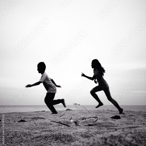 two kids running silhouettes running on the beach