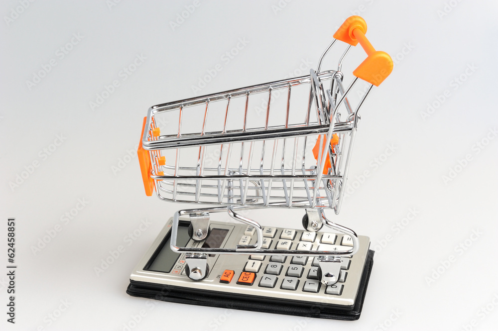 Shopping cart situated on calculator on gray