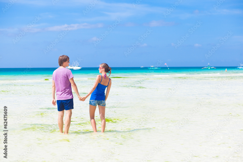 back view of couple holding hands in water on tropical beach in