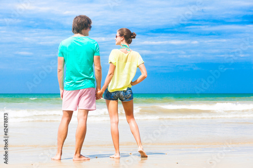 back view of couple holding hands on tropical beach in