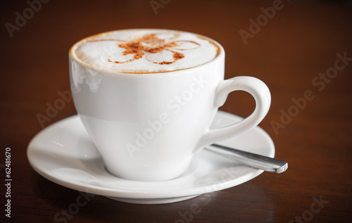 One white cup of cappuccino stands on dark wooden table