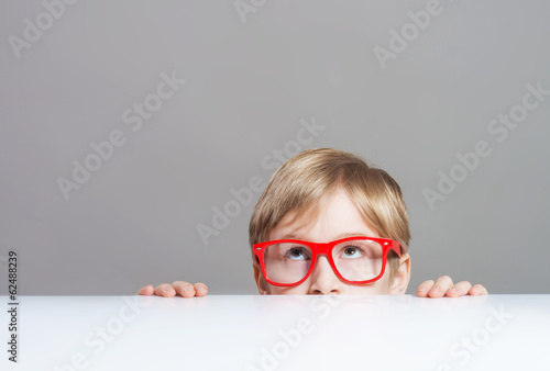 Boy in red-framed glasses looking up from behind the table