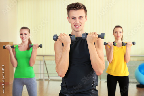 Young beautiful peoples engaged with dumbbells in gym