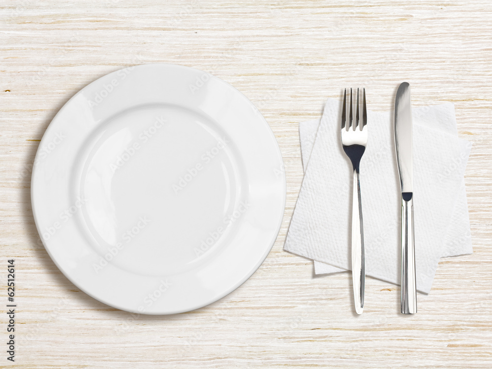 white plate, knife, fork and napkin top view on wooden table