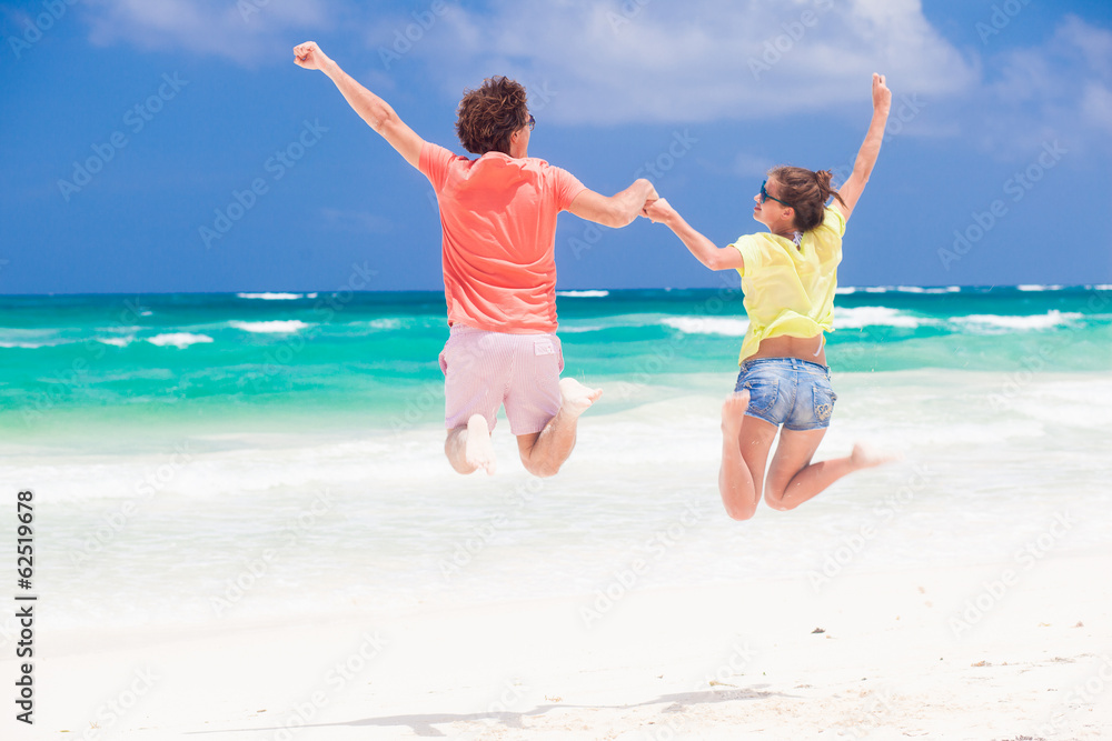 Young couple in bright clothes jumping on the beach looking on Young couple in bright clothes jumping on the beach looking on