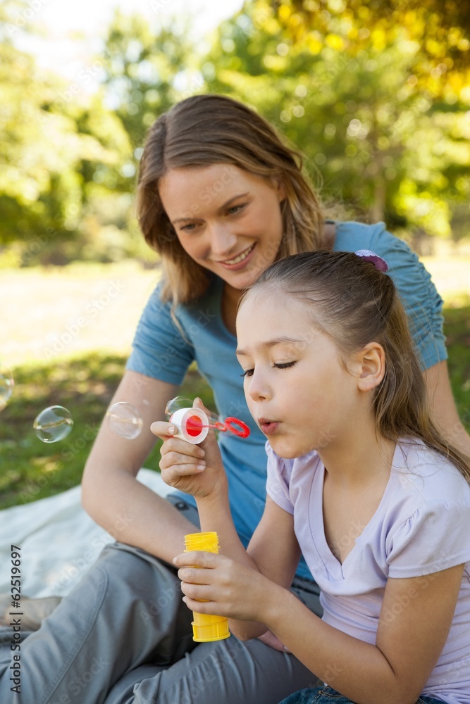 Mother with her daughter blowing soap bubbles at park Mother with her daughter blowing soap bubbles at park