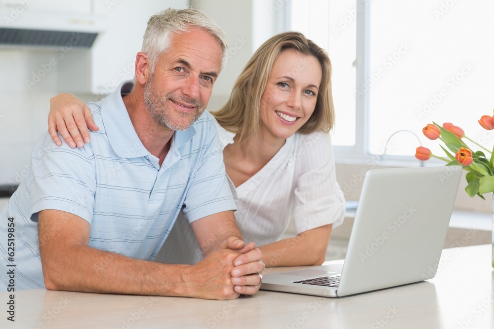 Cheerful couple using laptop together smiling at camera Cheerful couple using laptop together smiling at camera