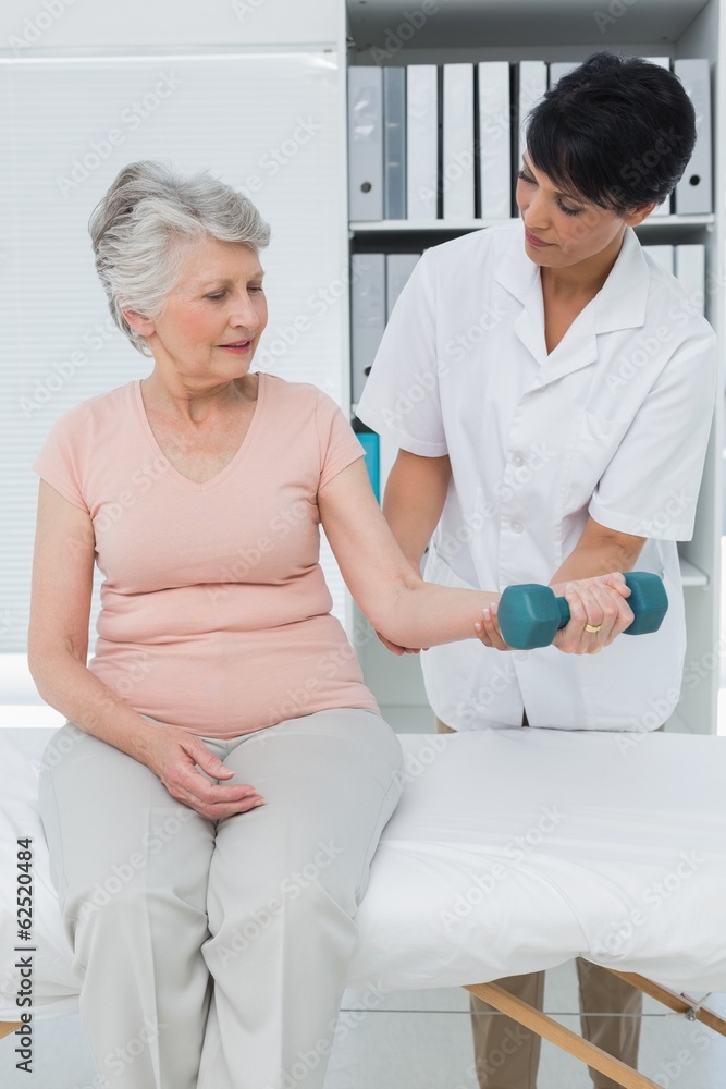 Physiotherapist assisting senior woman to lift dumbbell Physiotherapist assisting senior woman to lift dumbbell